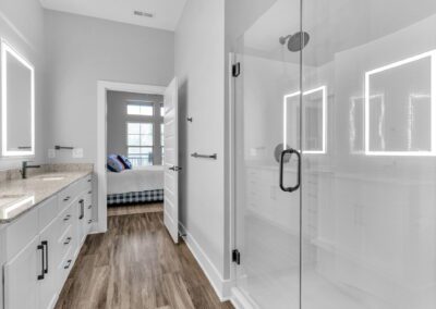 An en-suite bathroom with a double vanity, lighted mirrors, and a large glass-door shower with a rainfall shower head.