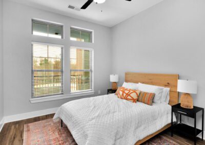 A rustic bedroom with orange decorative pillows on the bed and large windows with a view of the balcony outside.