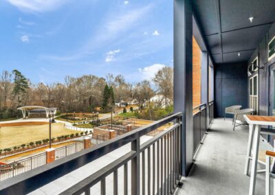 A balcony with steel, wood, and rattan patio furniture overlooking a grassy field