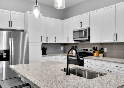 A clean white kitchen with a sink and barstools at the kitchen island. The appliances are stainless steel.