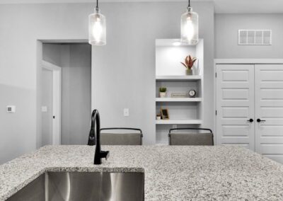 A kitchen island with an under-mount sink and barstools. Pendant lights hang above the island and built-in shelves are in the wall behind the seating.