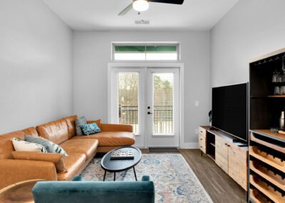 A small living room with white walls, a light brown leather sectional, and wooden furniture.