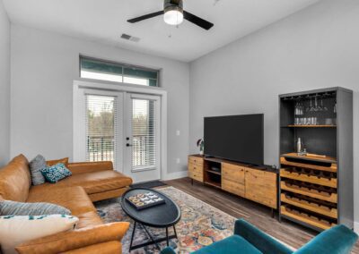 A small, rustic-style living room with white walls, a light brown leather sectional, and wooden furniture.